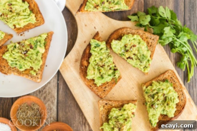 Avocado Toast 3 Overhead shot of two slices of freshly made avocado toast, topped with cilantro and red pepper flakes, placed on a wooden cutting board.