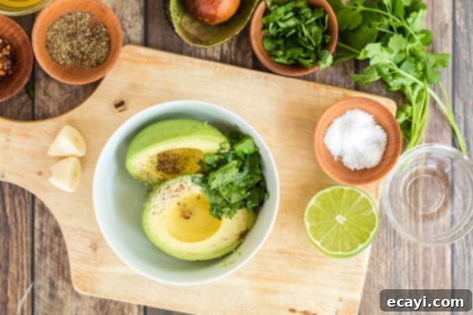 Avocado Toast 4 Ingredients for classic avocado toast arranged on a white surface: whole and halved avocados, fresh cilantro, a lime, sea salt, and black peppercorns.