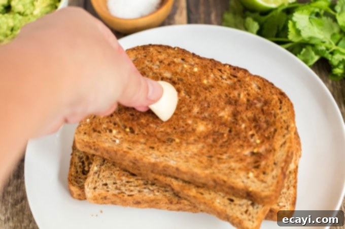 Avocado Toast 6 A hand rubbing a slice of golden-brown toast with a cut garlic clove, adding a subtle aromatic flavor.