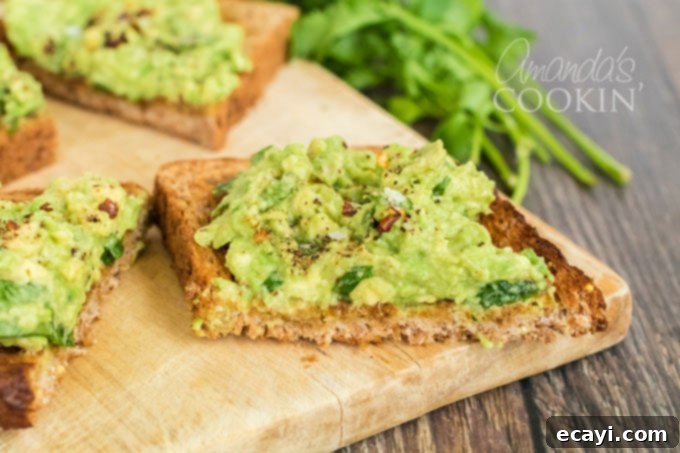 Avocado Toast 8 Close-up of a finished slice of avocado toast, garnished with fresh cilantro and red pepper flakes, with more cilantro in the soft-focused background.