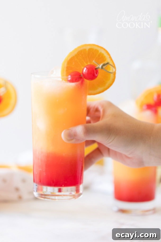 Enjoying a Freshly Made Tequila Sunrise Cocktail A hand holding a perfectly crafted Tequila Sunrise drink, showcasing the beautiful layered colors against a blurred background, inviting you to take a sip.