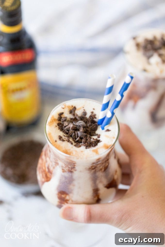 The Frozen Mudslide is a delicious combination of Kahlua coffee liqueur, Baileys Irish cream, vodka, and ice cream. It's a summertime cocktail dream. #mudslide #frozenmudslide #mudslidecocktail #summercocktails #frozenmudslidemilkshake #amandascookin hand holding glass of frozen mudslide