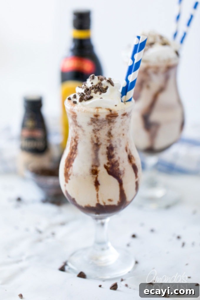 The Frozen Mudslide is a delicious combination of Kahlua coffee liqueur, Baileys Irish cream, vodka, and ice cream. It's a summertime cocktail dream. #mudslide #frozenmudslide #mudslidecocktail #summercocktails #frozenmudslidemilkshake #amandascookin two glasses of frozen mudslides with bottles in background