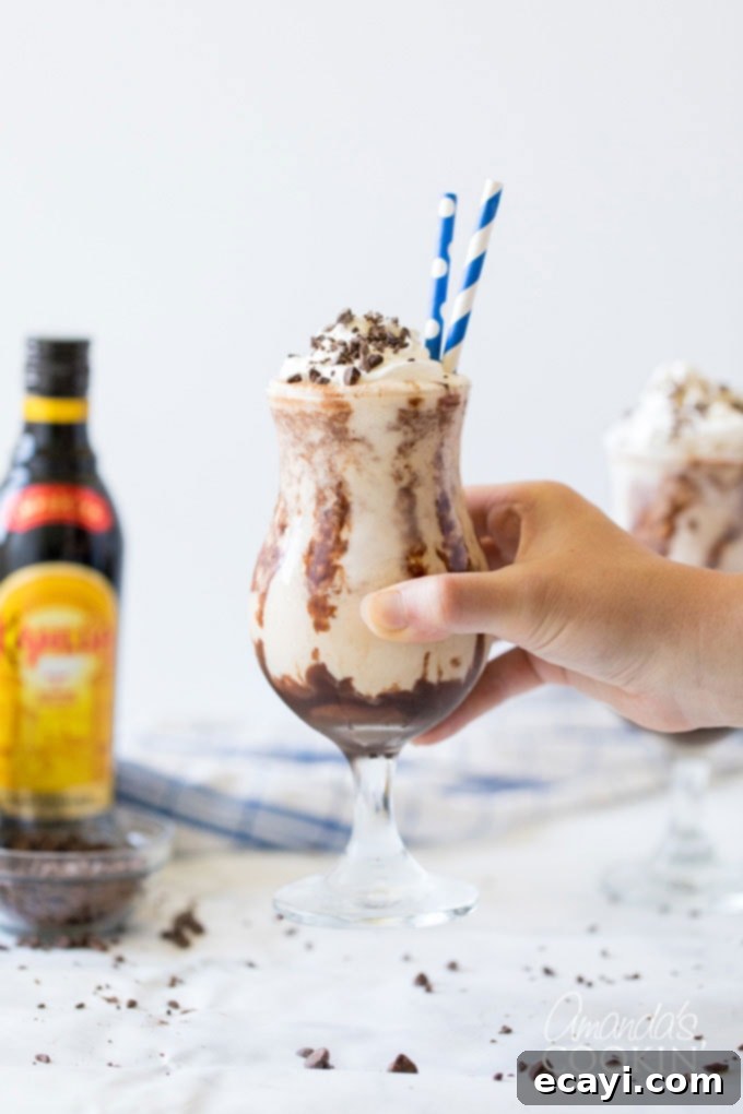 The Frozen Mudslide is a delicious combination of Kahlua coffee liqueur, Baileys Irish cream, vodka, and ice cream. It's a summertime cocktail dream. #mudslide #frozenmudslide #mudslidecocktail #summercocktails #frozenmudslidemilkshake #amandascookin holding glass of frozen mudslide