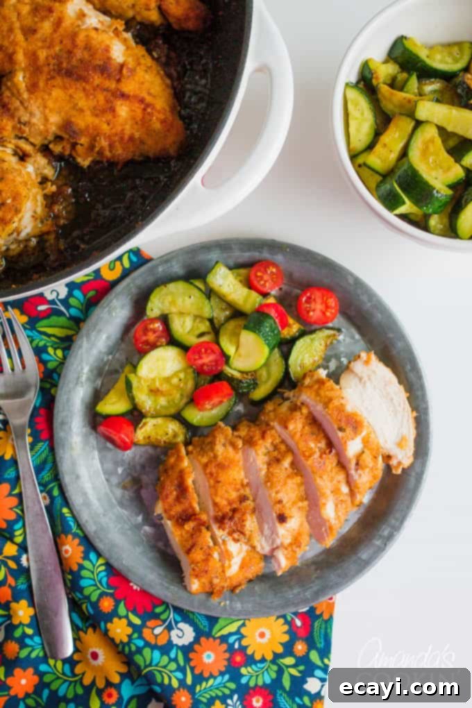 This spicy oven fried chicken gets its flavor from the spicy marinade. Be sure to marinate the chicken the suggested amount of time for perfect results! Sliced chicken on plate with zucchini and tomato side