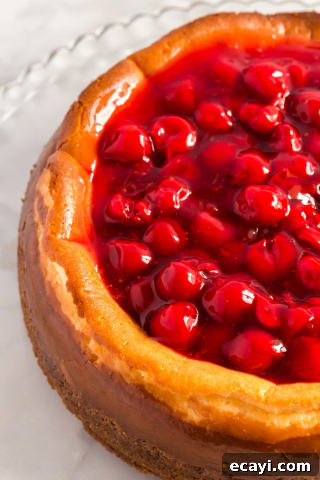 Decadent Cherry Cheesecake 3 Close-up view of the smooth, creamy surface of a whole cherry cheesecake, adorned with bright red cherry pie filling.
