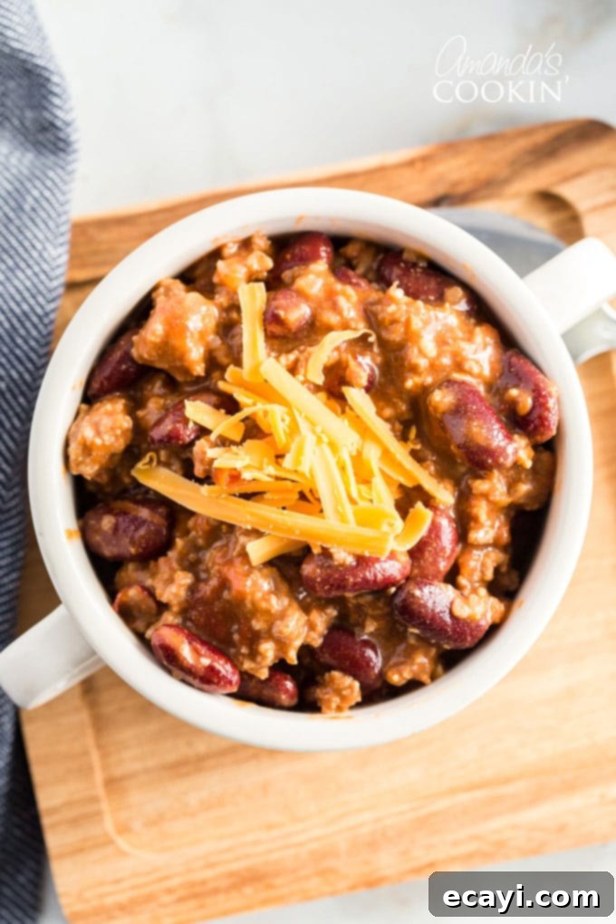 Classic Homemade Chili 10 Overhead view of a steaming bowl of homemade chili in a white bowl, garnished with cheese and green onions