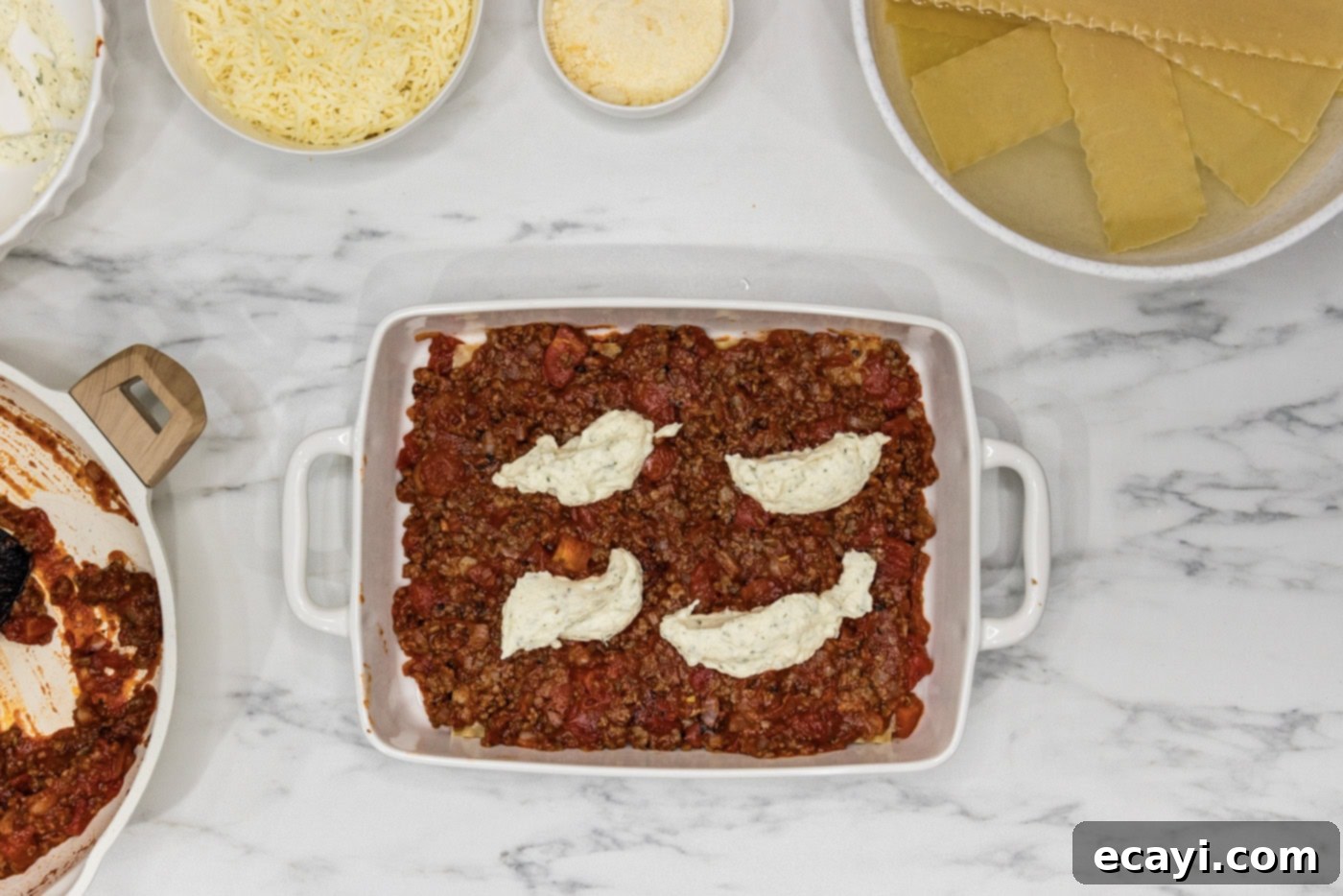 Classic Italian Lasagna 11 Small dollops of creamy ricotta cheese mixture spread over a layer of meat sauce and noodles in a baking dish, preparing for the next cheese layer.