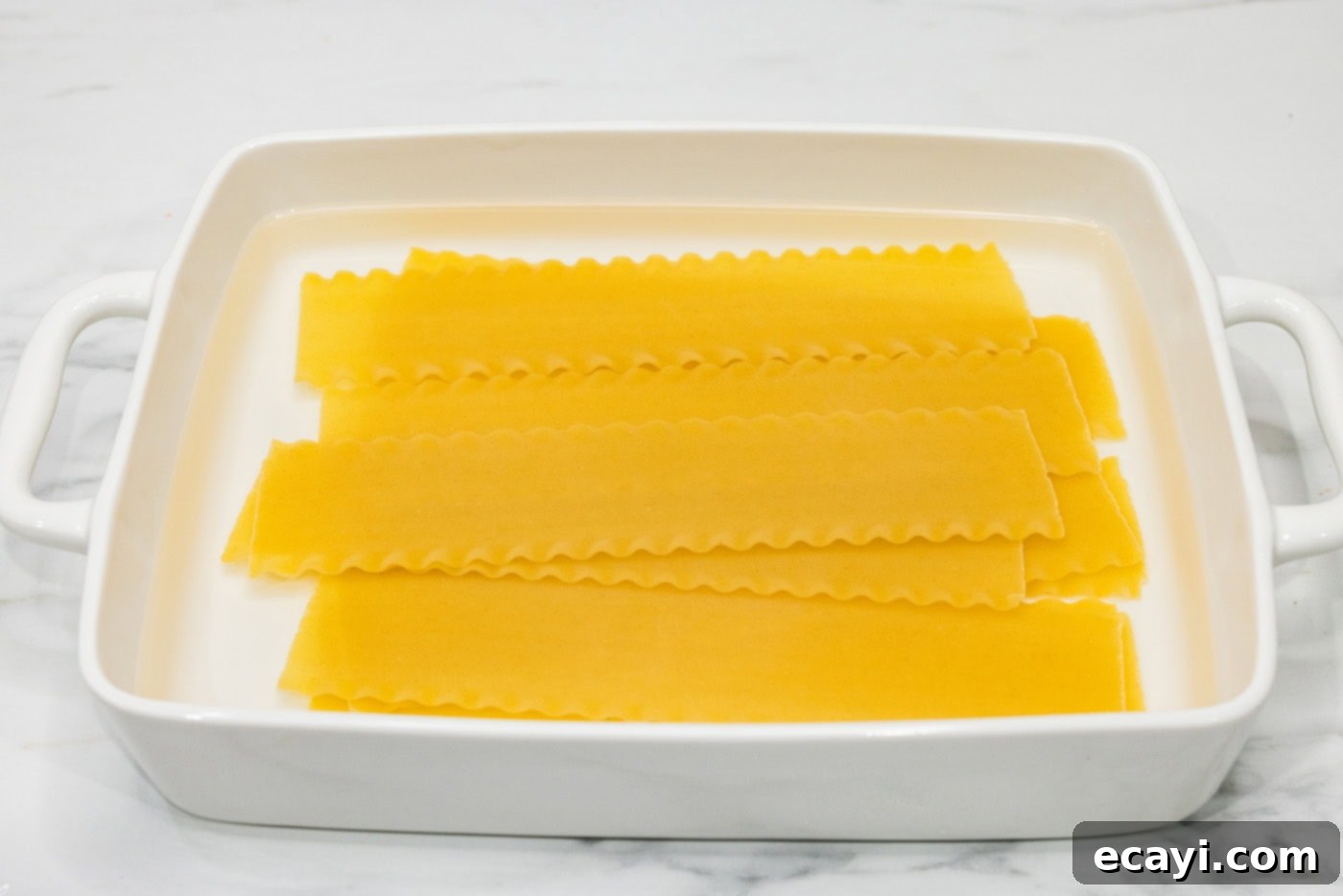 Classic Italian Lasagna 7 Lasagna noodles gently soaking in hot water within a baking dish, becoming pliable and ready for assembly.