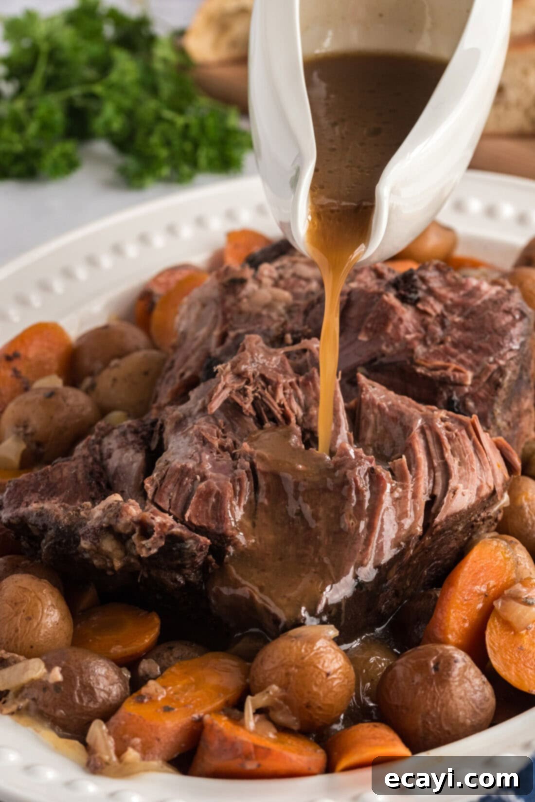 Melt-in-Your-Mouth Slow Cooker Pot Roast 3 Rich gravy being poured generously over slices of Crockpot Roast Beef on a serving platter, surrounded by cooked vegetables