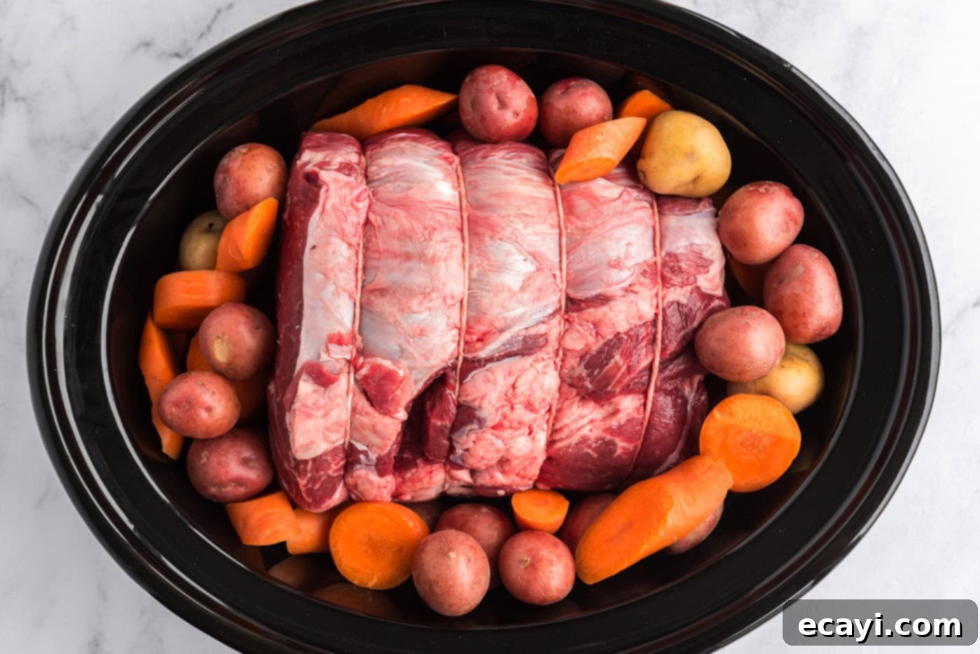 Melt-in-Your-Mouth Slow Cooker Pot Roast 7 Beef roast placed in the crockpot, surrounded by carrots and potatoes
