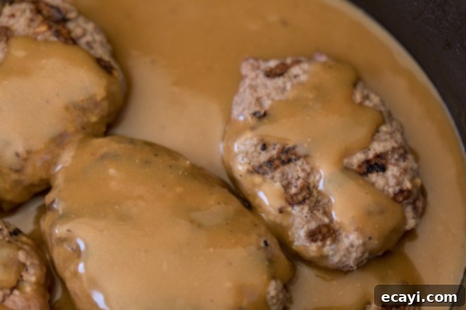Homestyle Salisbury Steaks 6 Close-up of Salisbury steaks cooking in a rich gravy in a skillet, showcasing the deep flavors.