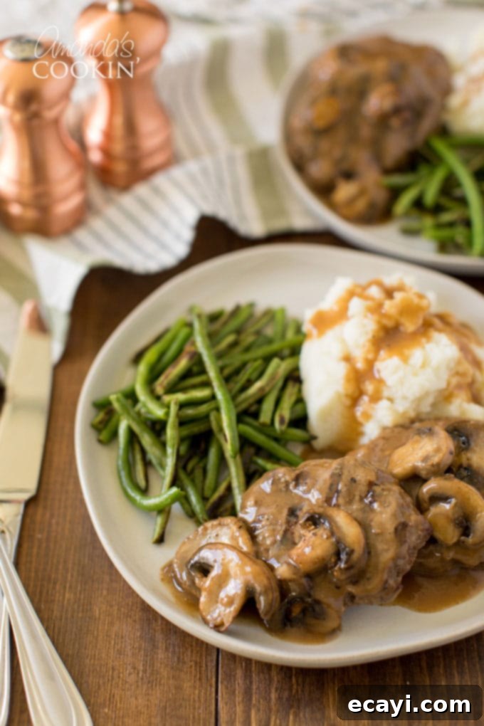 Enjoy these savory Salisbury Steaks, a recipe perfected over a decade, easily made in your slow cooker, oven, or skillet for a perfect family meal. A beautifully plated Salisbury steak dinner on a table, featuring the steak, gravy, and side dishes.