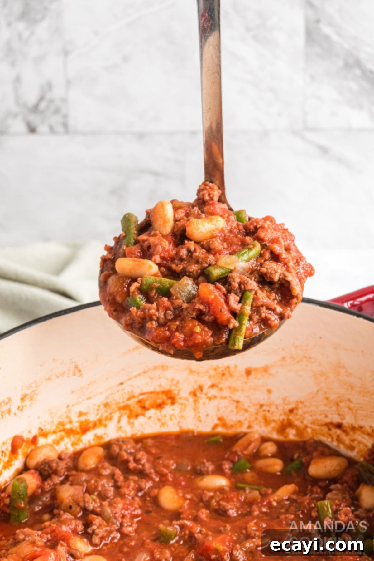 Hearty and Flavorful Italian Hamburger Stew Ready to Serve A ladle scooping a generous portion of Italian hamburger stew from a Dutch oven, showing the rich broth, ground meat, and vibrant vegetables.