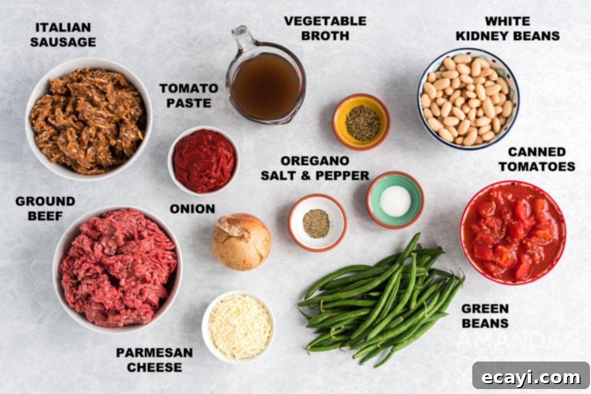 Hearty Ground Beef & Vegetable Stew 2 A flat lay photograph displaying all the fresh and pantry ingredients laid out and labeled for making Italian hamburger stew, including ground beef, Italian sausage, onion, cannellini beans, green beans, canned tomatoes, vegetable broth, tomato paste, oregano, salt, pepper, and Parmesan cheese.