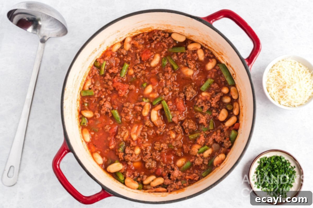 Hearty Italian Hamburger Stew Simmering to Develop Rich Flavors A Dutch oven of Italian hamburger stew gently simmering with a rich red broth, tender green beans, and cannellini beans visible, indicating deep flavors.