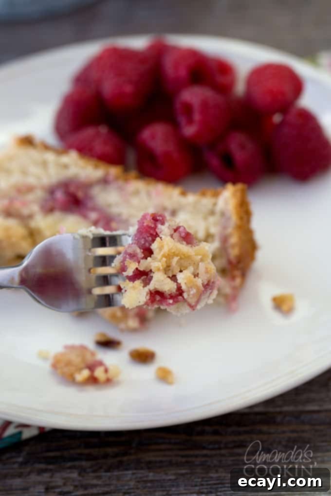 Tangy Raspberry Swirl Coffee Cake 3 A close-up shot of a fork taking a bite of raspberry coffee cake, with a slice visible in the soft-focus background.