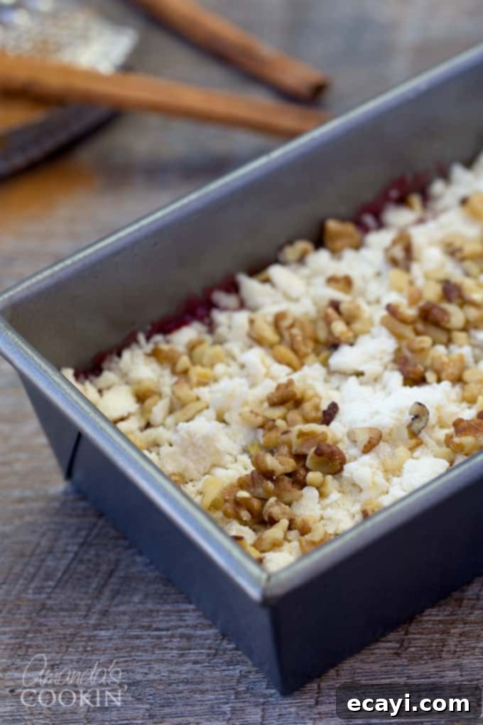 Tangy Raspberry Swirl Coffee Cake 8 A close-up view of a loaf pan filled with coffee cake batter, raspberry filling, a generous crumb topping, and scattered chopped walnuts.