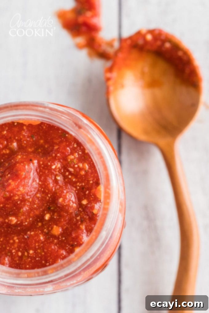 How to make homemade pizza sauce. You likely have all the ingredients in your pantry! Learn how to make your own pizza sauce and freeze it for later too! close up of jar of homemade pizza sauce with a spoon on the side