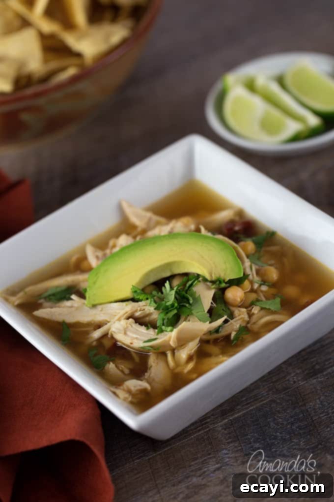 Chipotle Chicken Comfort Bowl 2 A close up of a square white bowl filled with chipotle chicken soup, topped with one slice of avocado.