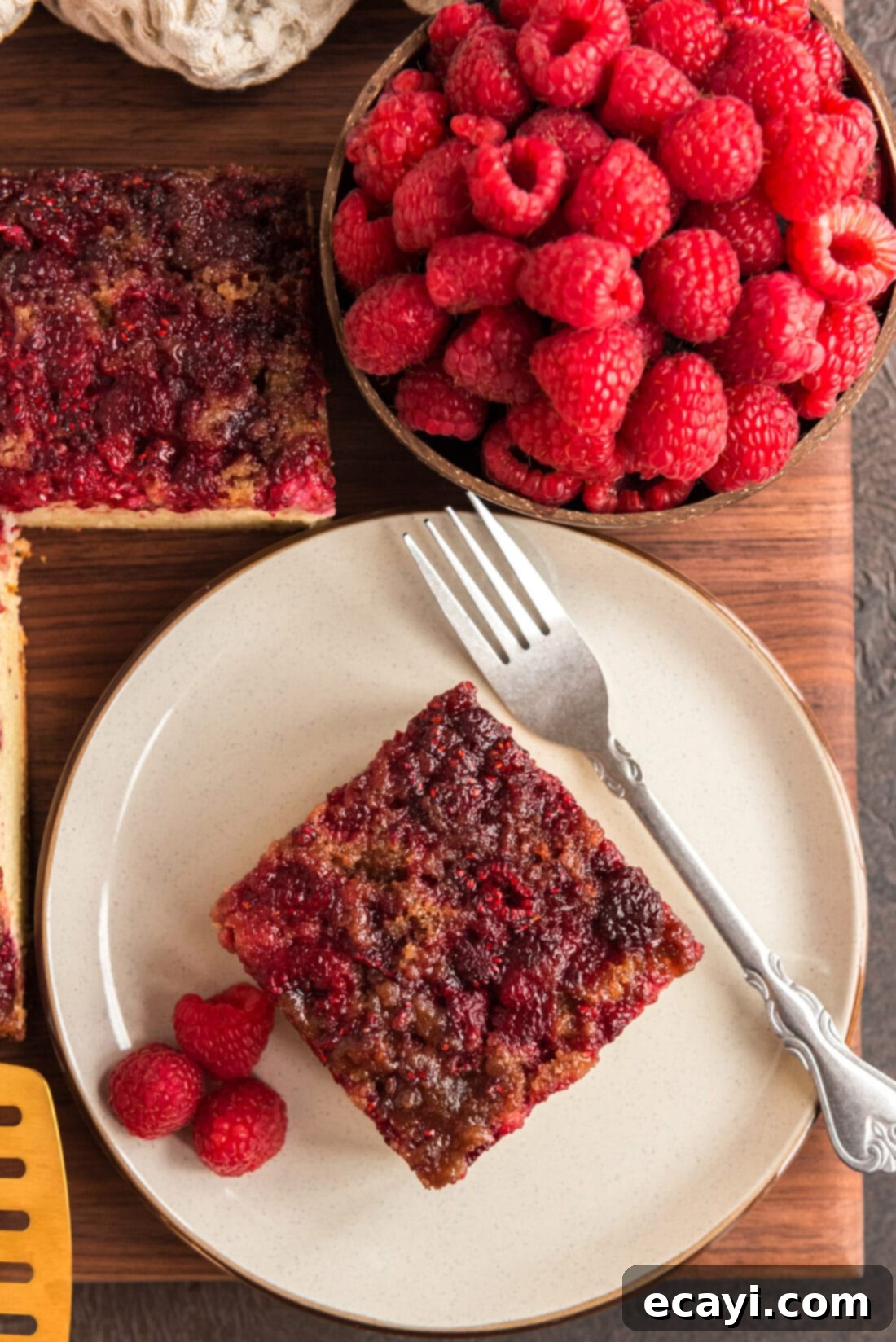 Ruby Raspberry Reveal 3 Square of Raspberry Upside Down Cake on a plate with a bowl of raspberries next to it