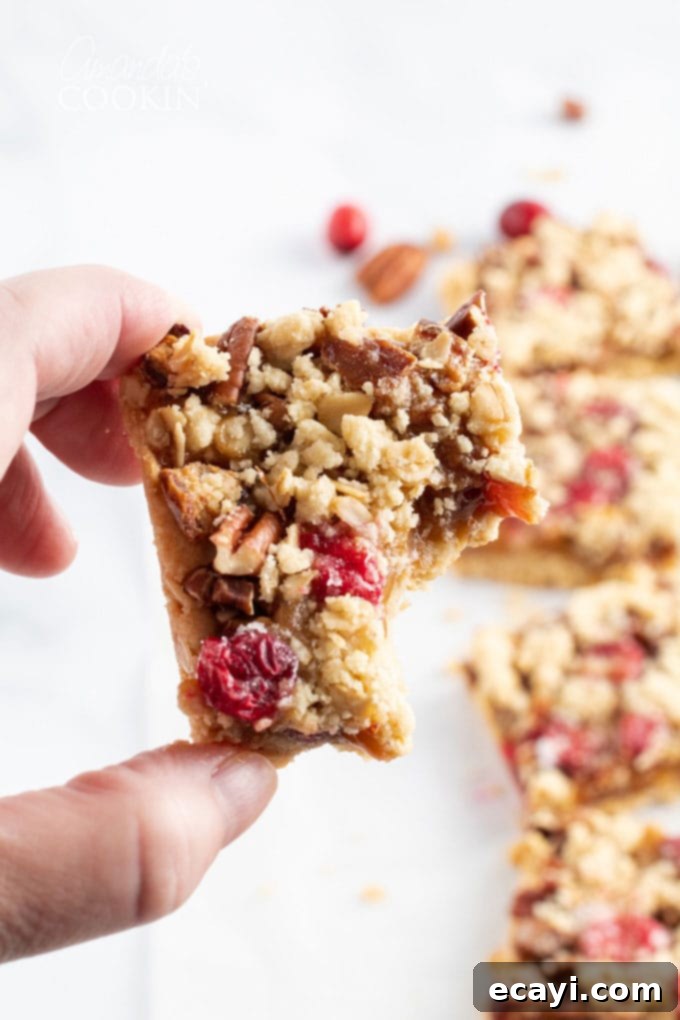 Caramel Cranberry Bliss Bars 3 a cranberry caramel bar with a bite taken out, revealing the delicious layers of oats, cranberries, and caramel