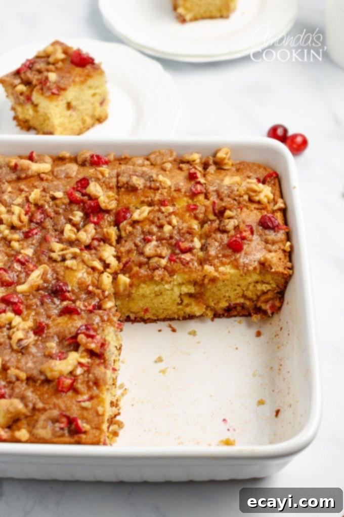 Cranberry Coffee Cake is filled with plump cranberries and topped with a delicious streusel topping. This is an easy to make coffee cake for Christmas. A pan of Cranberry Coffee Cake with several squares already removed, showcasing its moist interior and streusel topping.