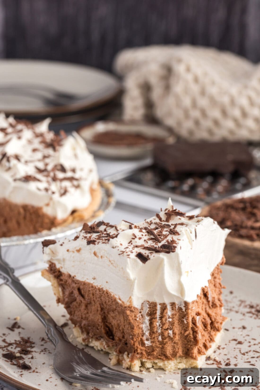 Silky Chocolate Dream 2 A perfect slice of French Silk Pie on a white plate, showcasing its rich chocolate filling, tall whipped cream topping, and a sprinkle of chocolate shavings. A small bite has been removed.