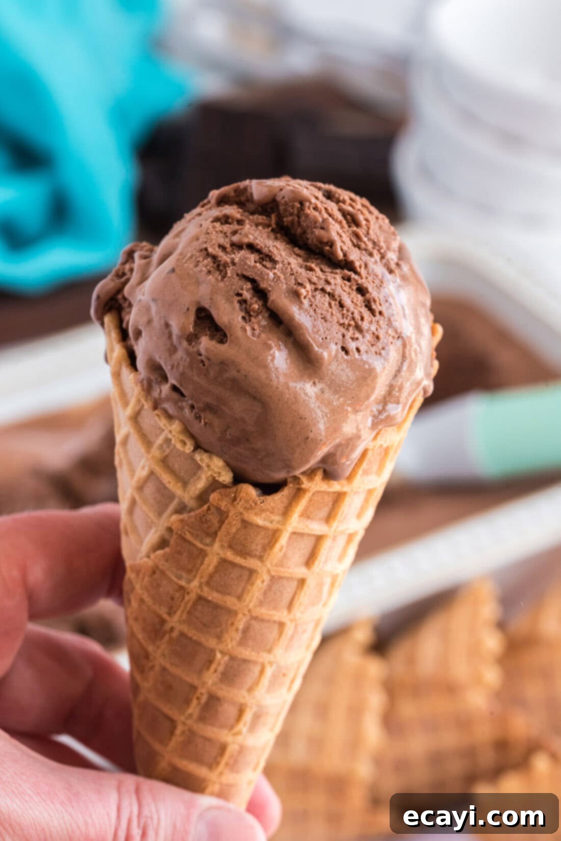 Decadent Homemade Chocolate Ice Cream 17 Hand holding a cone of Homemade Chocolate Ice Cream with rainbow sprinkles against a bright background