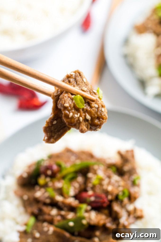 Khan's Caramel Beef 3 chop sticks holding a piece of mongolian beef over a bowl of rice, highlighting the tender beef
