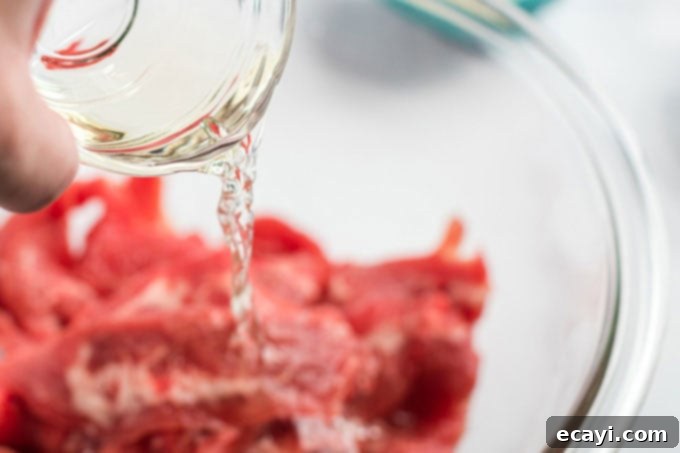 Khan's Caramel Beef 5 sherry cooking wine pouring over thinly sliced beef in a bowl for marination
