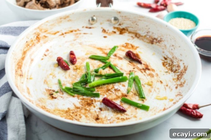 Khan's Caramel Beef 8 chili peppers and green onions stir-frying in a skillet, releasing aromatic flavors