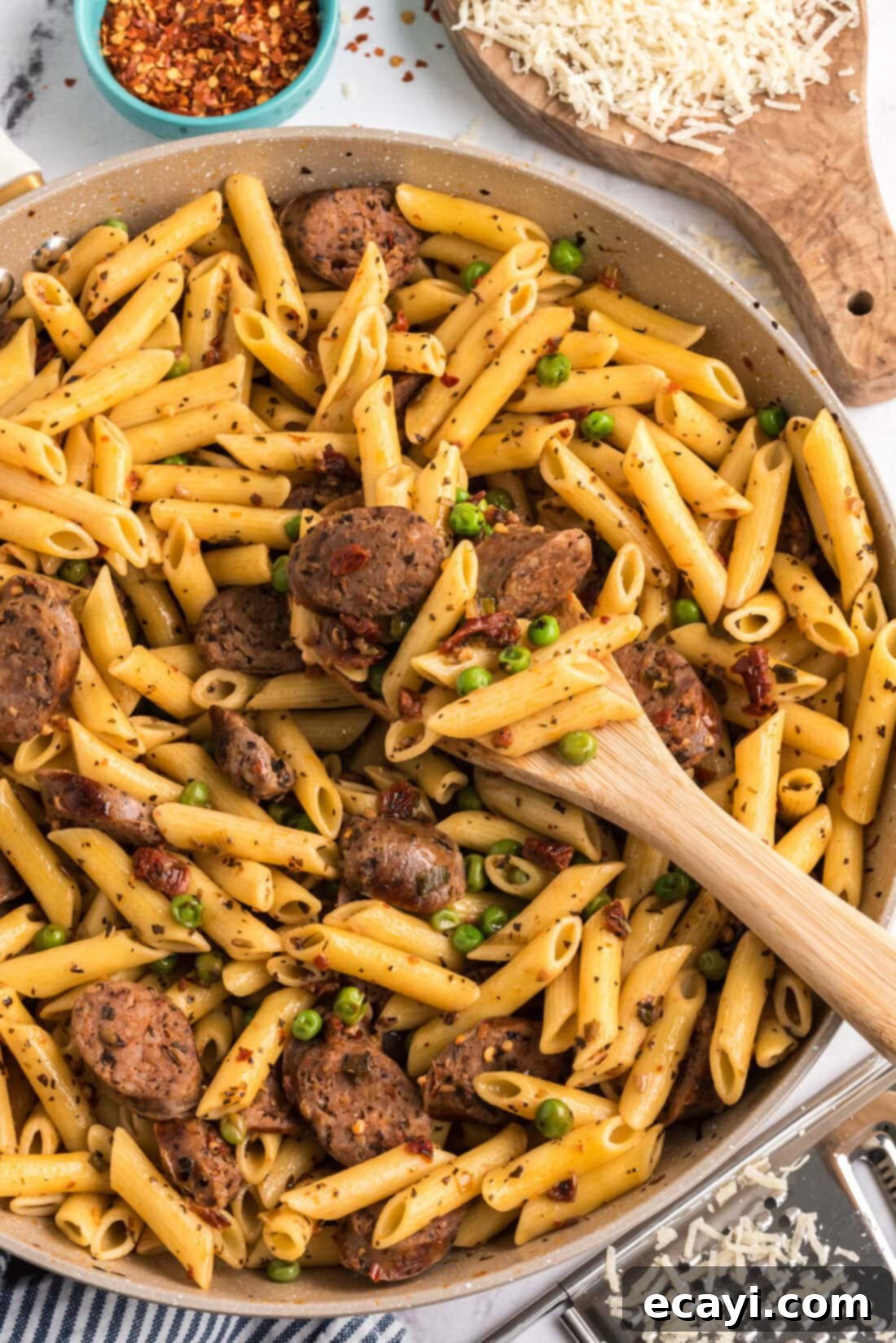 Hearty Sausage Penne With Peas 2 Sausage, Penne & Peas in a skillet with a spoon, highlighting the rich colors of the dish.