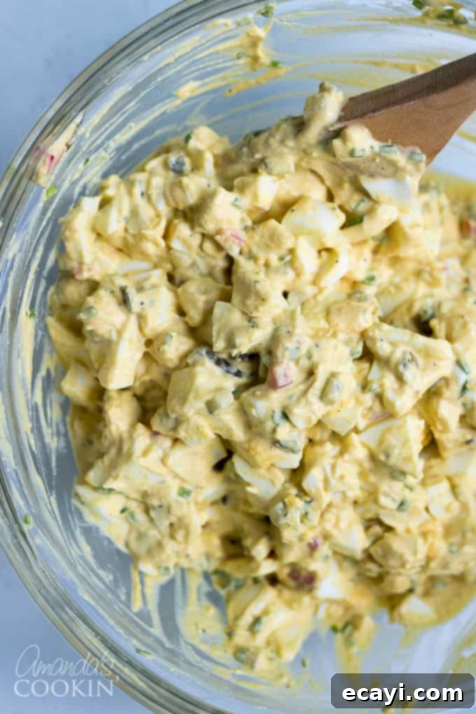 Mix together egg salad ingredients for the best flavor and texture. Ideal for any potluck or BBQ! Thoroughly mixing together egg salad ingredients in a bowl for a uniform texture.
