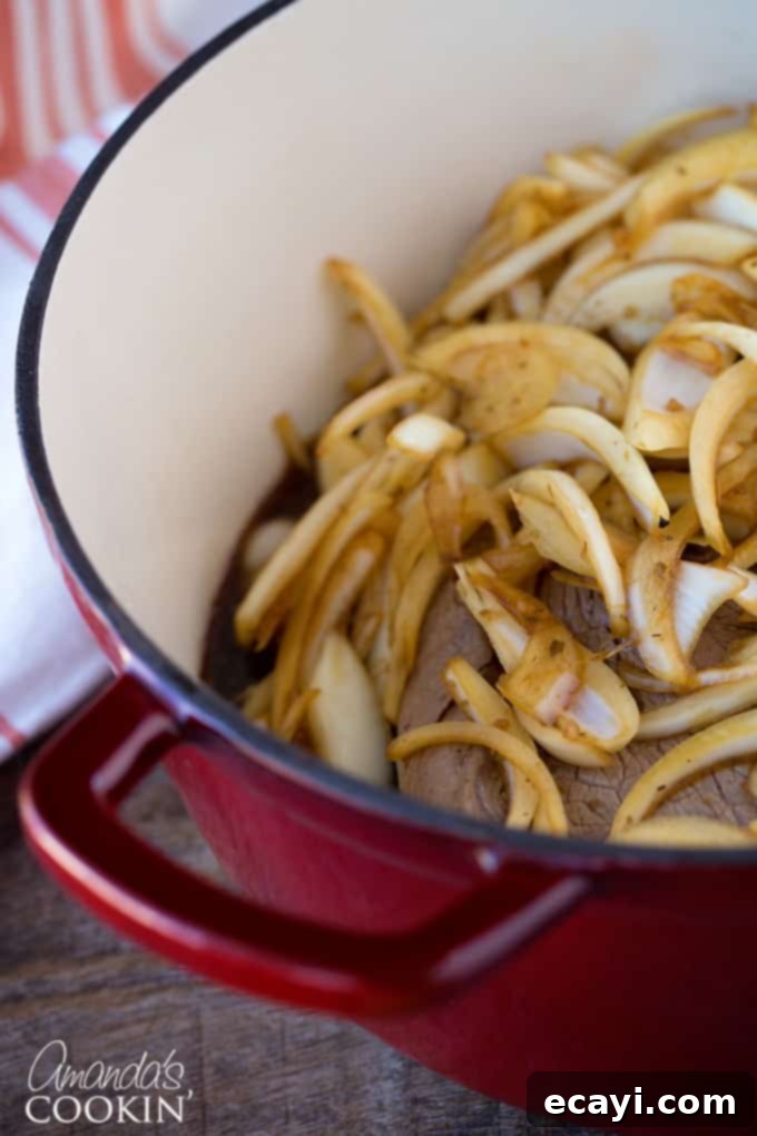 Traditional Amish Pot Roast 6 Dutch oven with pot roast, strategically topped with half of the sliced onions and the other half in the savory sauce.