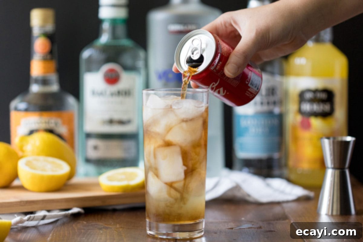 No Tea, All Buzz 5 A hand pouring cola into a highball glass already containing the mixed spirits and ice for a Long Island Iced Tea, creating its characteristic amber color.