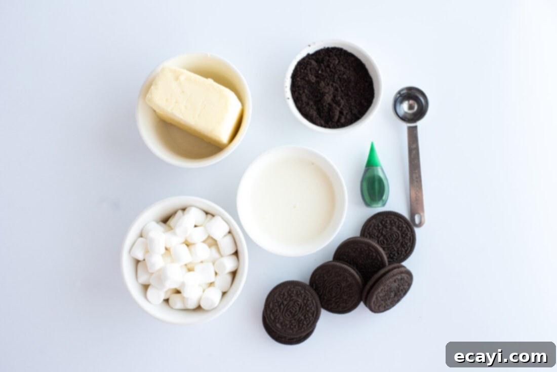 Decadent Grasshopper Pie 4 A collection of the 7 simple ingredients laid out on a white surface, including graham cracker crumbs, butter, marshmallows, heavy cream, peppermint extract, green food coloring, and Oreos, ready to make Grasshopper Pie.