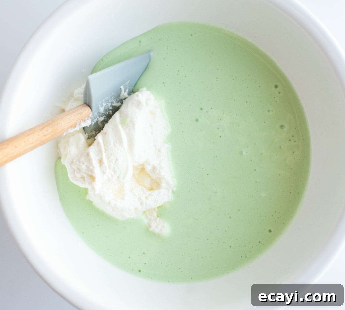 Decadent Grasshopper Pie 8 Green food coloring and peppermint extract being stirred into the melted marshmallow and heavy cream mixture, giving it a vibrant mint color.