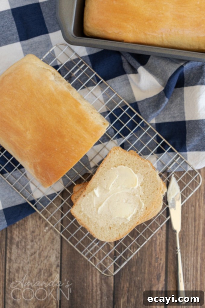 Homemade Amish white bread is ideal for sandwiches, French toast, grilled cheese, or your breakfast toast. Warm homemade bread is great with dinner too! Overhead view of a loaf of Amish white bread with a buttered slice next to it, showcasing its soft texture