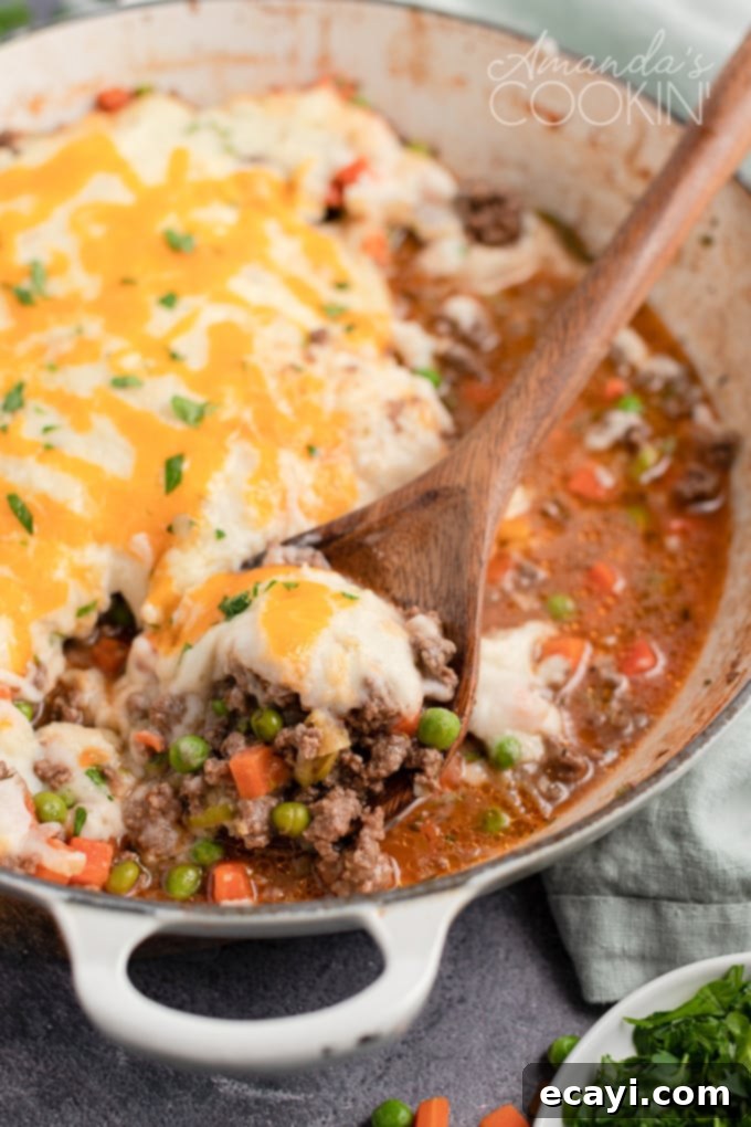 This Shepherd's Pie uses fresh ingredients mixed with ground beef to make a deliciously satisfying and filling dinner recipe! Spoon lifting Shepherd's Pie from a pan, showing the mashed potato topping and rich filling.
