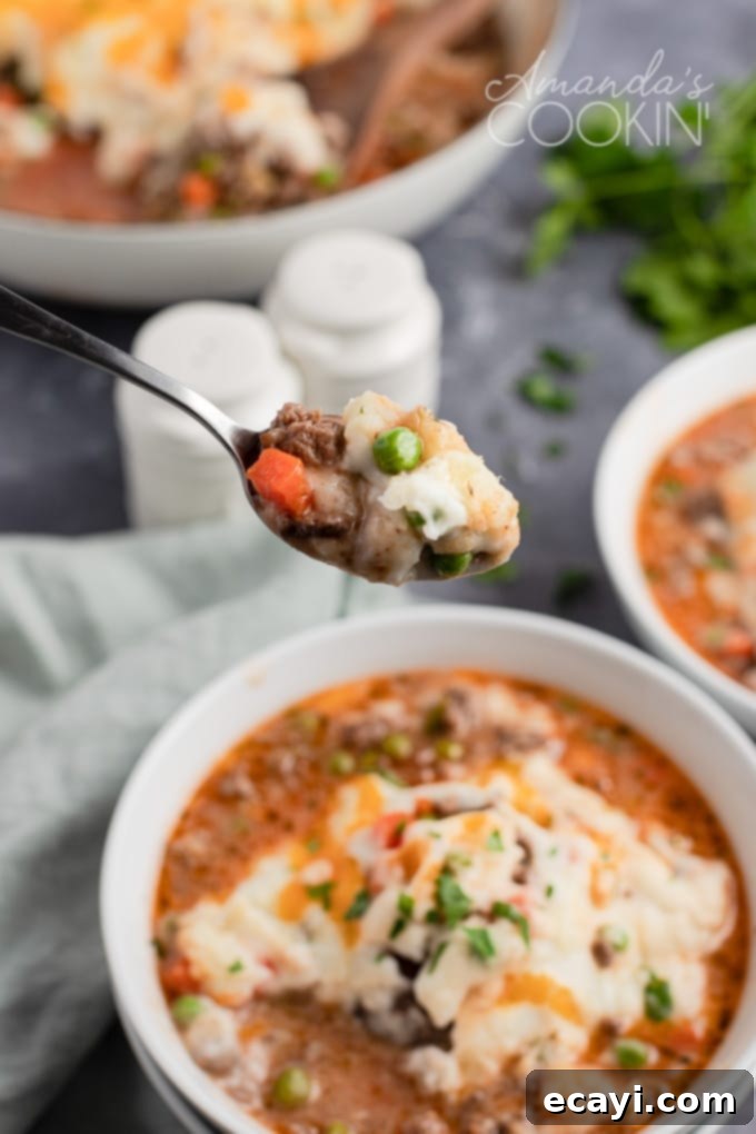 This Shepherd's Pie uses fresh ingredients mixed with ground beef to make a deliciously satisfying and filling dinner recipe! Spoon with a portion of Shepherd's Pie, showing the layers of meat and mashed potato.