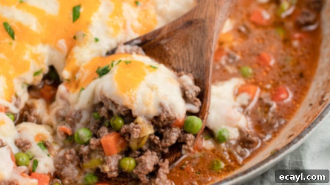 This Shepherd's Pie uses fresh ingredients mixed with ground beef to make a deliciously satisfying and filling dinner recipe! Close-up of Shepherd's Pie in a wooden spoon, highlighting the rich texture.