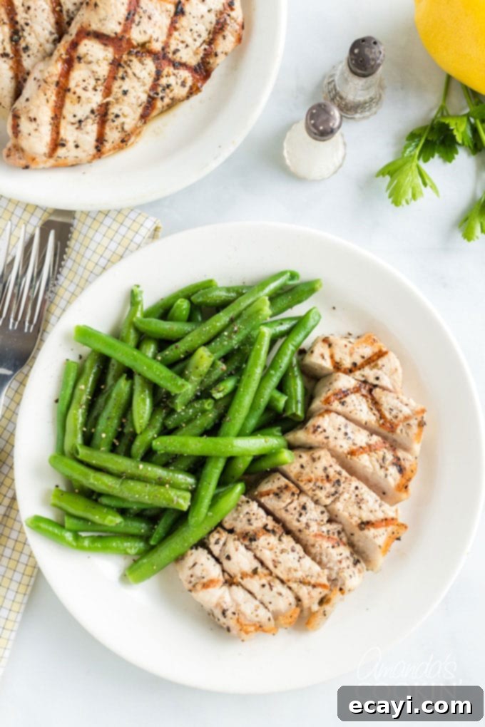Discover how to make the ultimate grilled pork chops. This easy recipe with lemon, olive oil, garlic, and fresh herbs guarantees a flavorful and tender meal. A perfectly cooked, sliced pork chop served on a plate alongside fresh green beans, highlighting its tender, juicy interior.