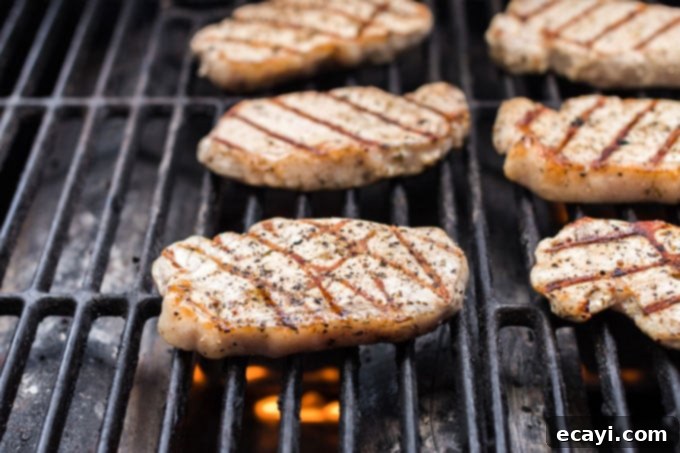 Watch your pork chops sizzle and develop perfect grill marks on the hot grill, building incredible flavor. Three juicy pork chops sizzling on a hot grill, showing developing grill marks and a golden-brown crust.