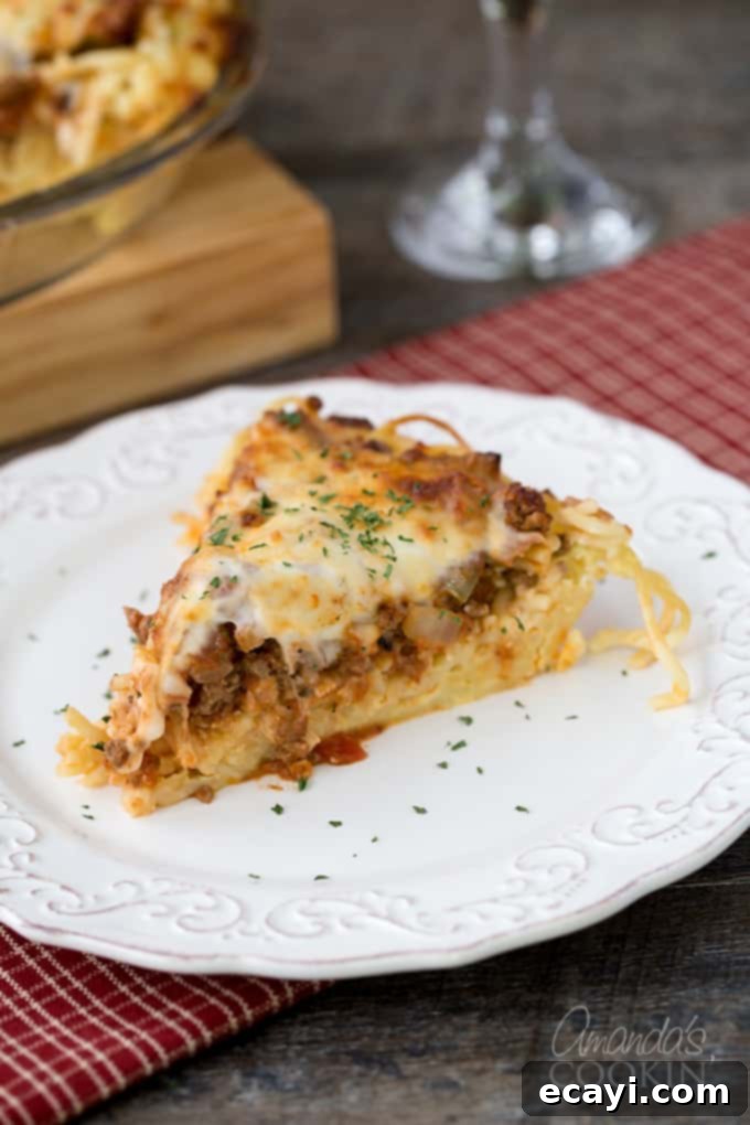Pasta Pie Perfection 2 A perfectly portioned slice of golden-brown spaghetti pie, showcasing its distinct layers of pasta, creamy filling, and savory meat sauce, served on a crisp white plate.