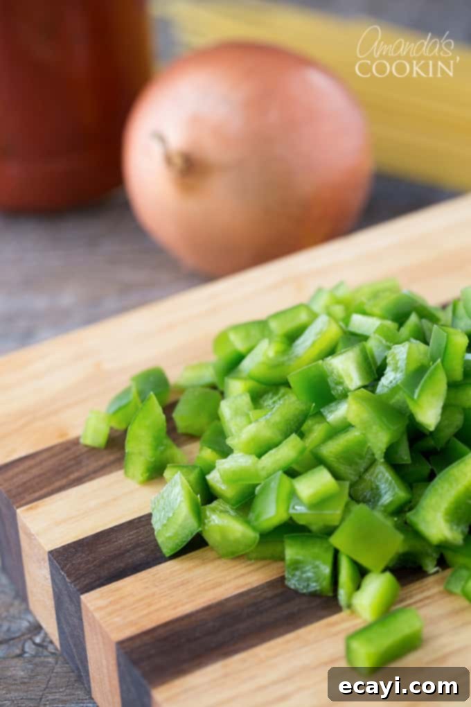 Pasta Pie Perfection 4 Freshly chopped vibrant green bell pepper rests alongside a mound of diced onion on a rustic wooden cutting board, all prepped and ready to be added to the savory meat sauce.