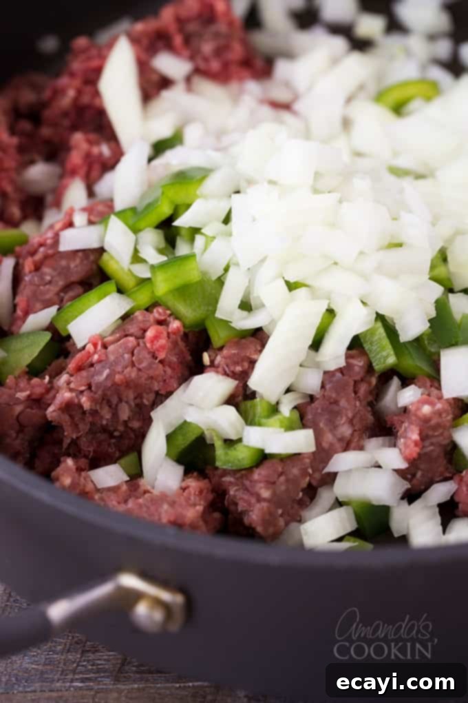 Pasta Pie Perfection 5 A close-up shot of lean ground beef, finely chopped green bell pepper, and diced onion sizzling and browning together in a non-stick skillet, forming the savory base of the spaghetti pie filling.