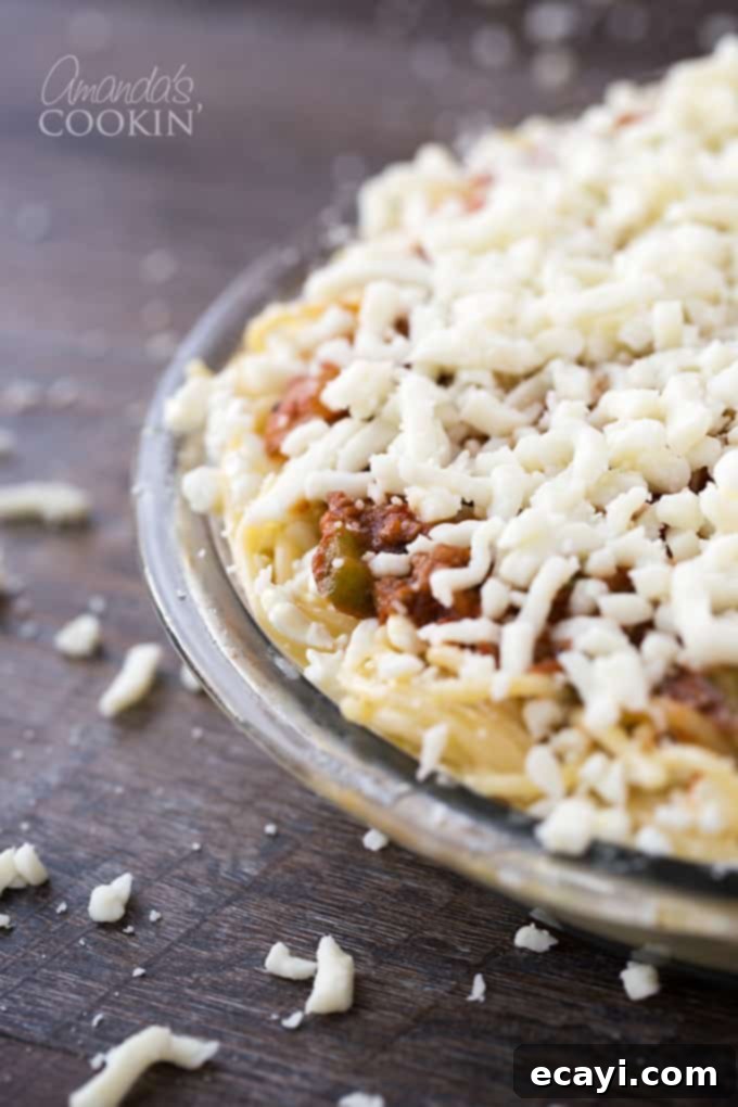 Pasta Pie Perfection 7 An assembled spaghetti pie in a clear glass dish, beautifully layered with the spaghetti crust, creamy cottage cheese, meat sauce, and generously topped with shredded mozzarella cheese, glistening and ready for the oven.