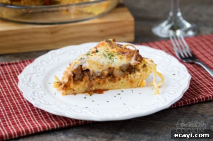 Pasta Pie Perfection 8 A close-up shot of a single, appetizing slice of spaghetti pie on a white plate, revealing the distinct and delicious layers of pasta crust, creamy cheese filling, and hearty meat sauce, with a melted cheese topping.