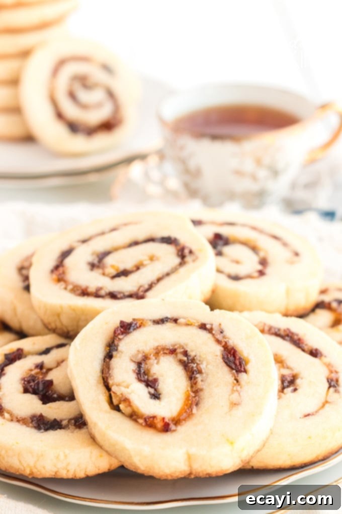 Cranberries, pecans, and orange marmalade are used as a filling and the dough is rolled up jelly-roll style to make these Cranberry Orange Spiral Cookies. A plate full of beautifully arranged cranberry orange spiral cookies, showcasing their intricate red and orange swirls against the golden cookie.